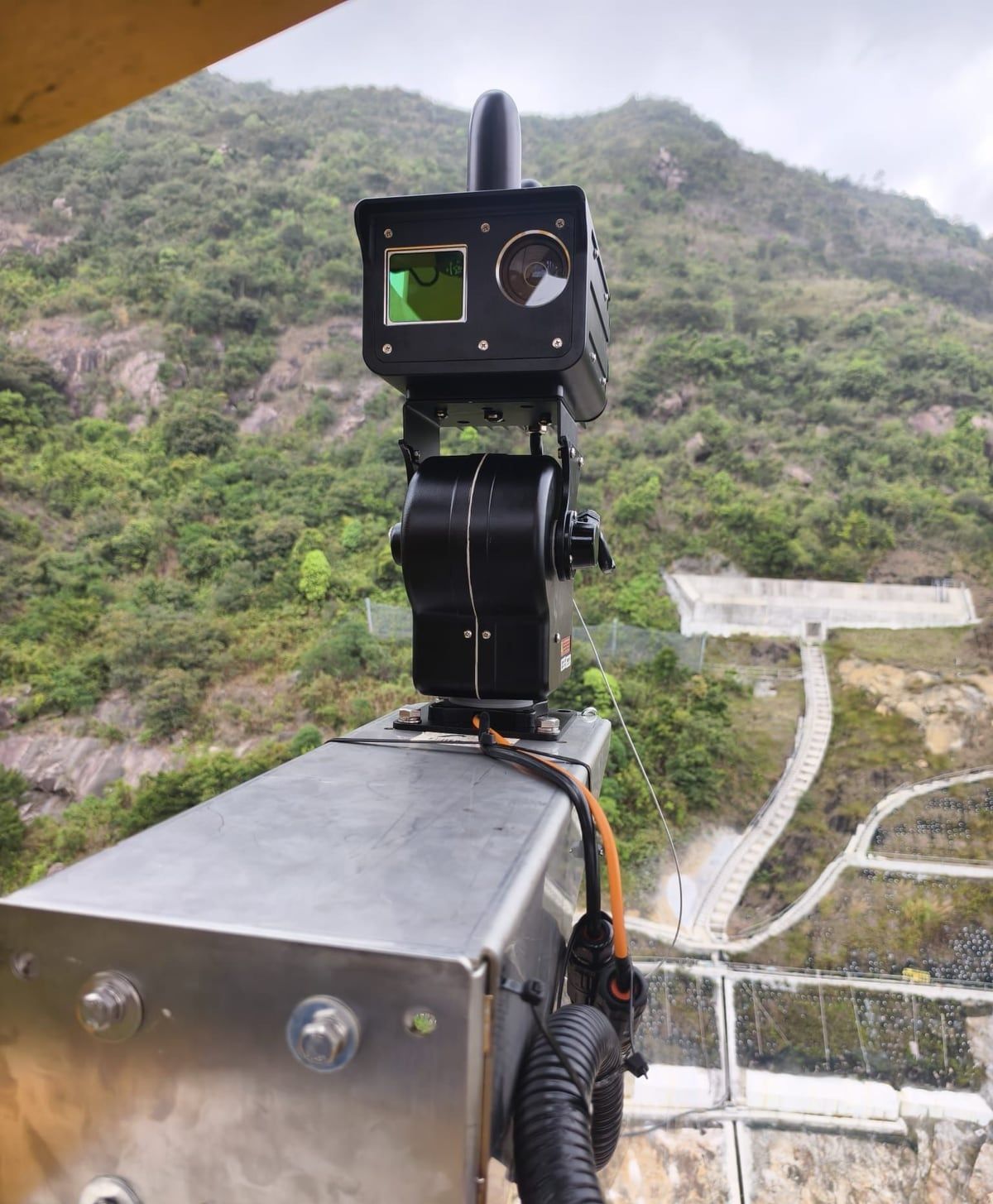 A Kodifly LiDAR and camera unit on a pan-tilt head, facing a hillside works site